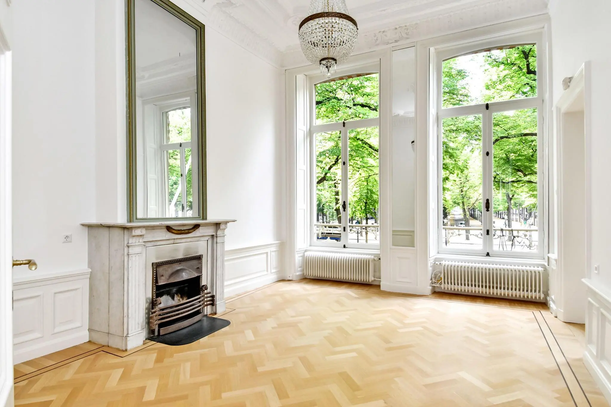 Lichte, klassieke kamer aan het Lange Voorhout met hoge ramen, visgraatvloer en marmeren schouw.